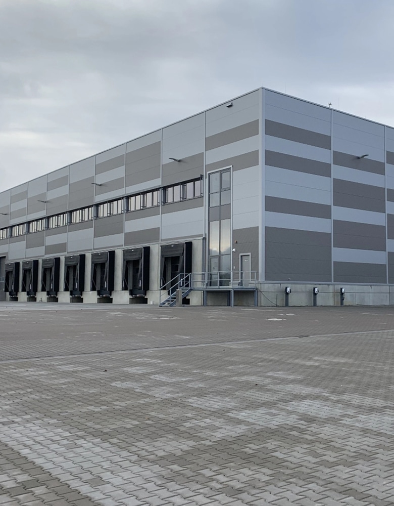 a grey industrial building sits vacant, the loading docks are covered in black and are lined up perfectly