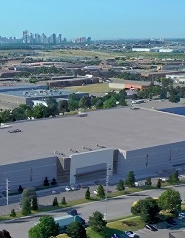 Aerial view of Courtney Park, an industrial area with large warehouses, loading docks, surrounding roads, parked vehicles, and a distant city skyline with high-rise buildings