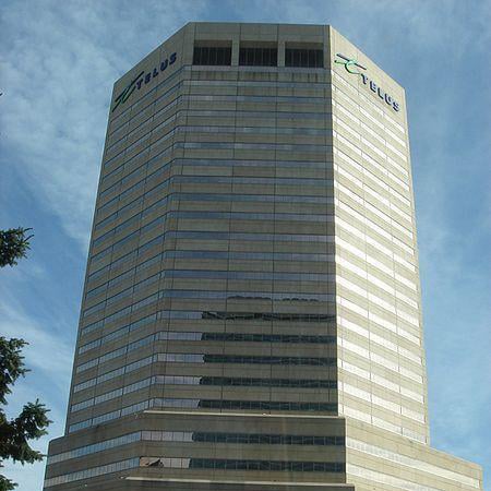 Tall office building with the TELUS logo displayed on two sides near the top, featuring numerous windows and a reflective glass exterior
